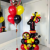 Mickey-themed balloon setup with red, yellow, and black number stack, helium bouquet, and personalized name decal