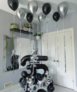 Black and silver balloon number stack with star accents and helium balloons with tassels for a modern birthday setup