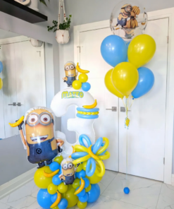 Minions-themed balloon setup with blue and yellow number stack, banana accents, helium bouquet, and personalized name decal