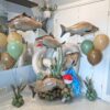 Fishing themed balloon setup with number stack, large fish balloons, cattails, and neutral green and tan colours for birthday display