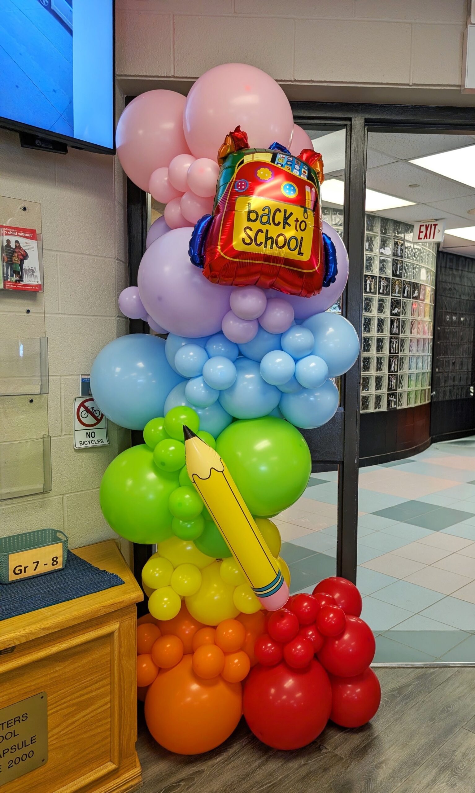 Colourful back-to-school balloon column with backpack balloon, oversized pencil and rainbow balloon clusters.