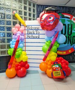 Rainbow back-to-school balloon display with a custom welcome backdrop, pencil, crayon, apple and backpack balloons.