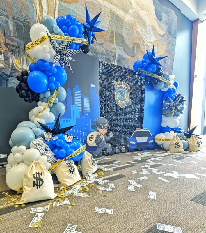 Blue, black and white organic balloons framing a police chase backdrop with themed props.