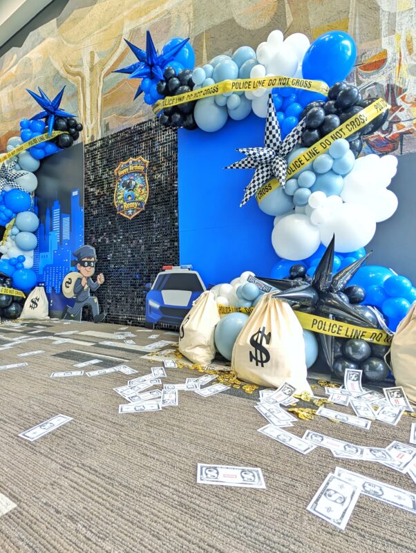 Police-themed balloon backdrop with shimmer wall, money bags, caution tape and robber cutout.