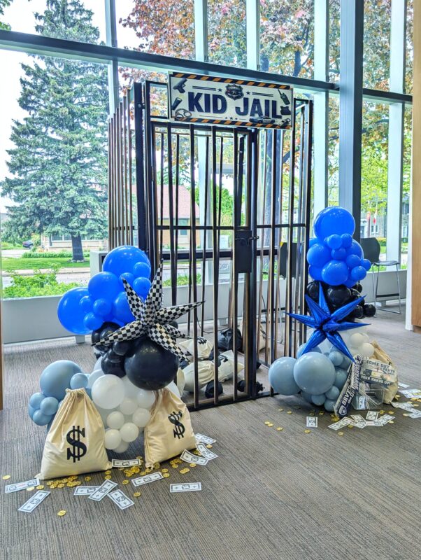 Custom Kid Jail photo prop with blue, black and white balloons inside the library lounge.