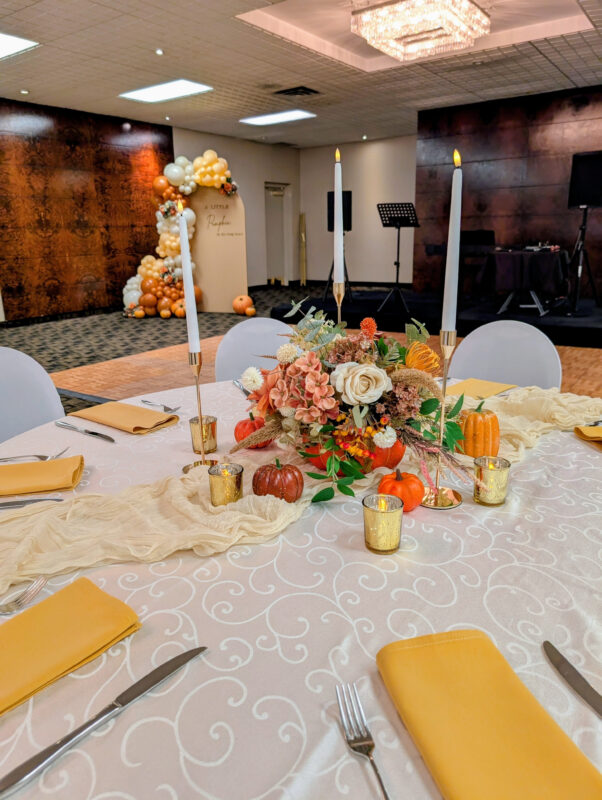 Pumpkin floral centrepiece with warm faux blooms, candles and seasonal table accents.
