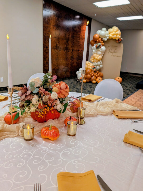 Fall baby shower table with pumpkin florals, gold candles, mustard napkins and a cream runner.