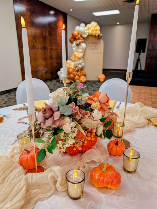 Elegant autumn baby shower tablescape with faux florals, pumpkins, candles and a ripple wall backdrop.