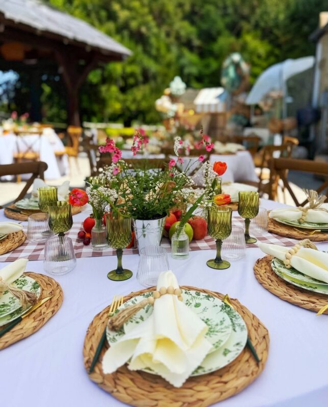 Garden-inspired place setting with woven charger, green glassware, florals and folded ivory napkin.