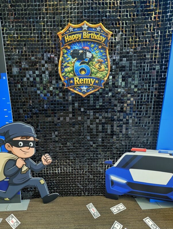 Personalized police badge on a black shimmer wall with robber and police car cutouts.
