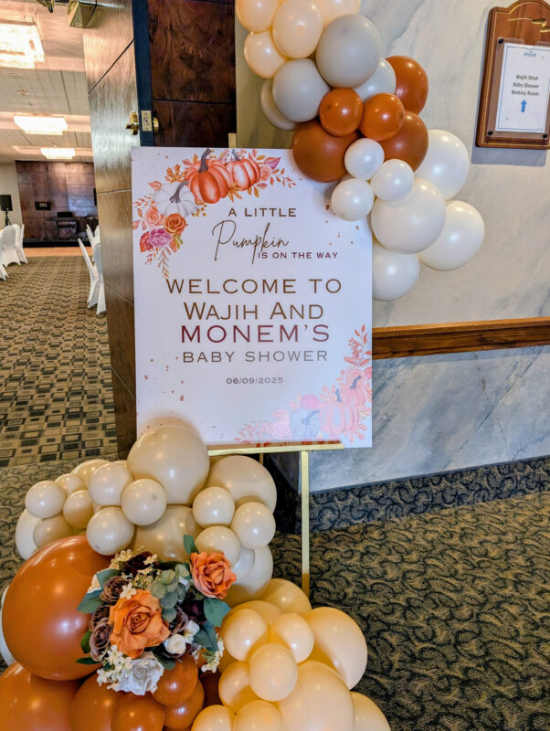Close view of a personalized little pumpkin baby shower sign framed by an organic balloon display.