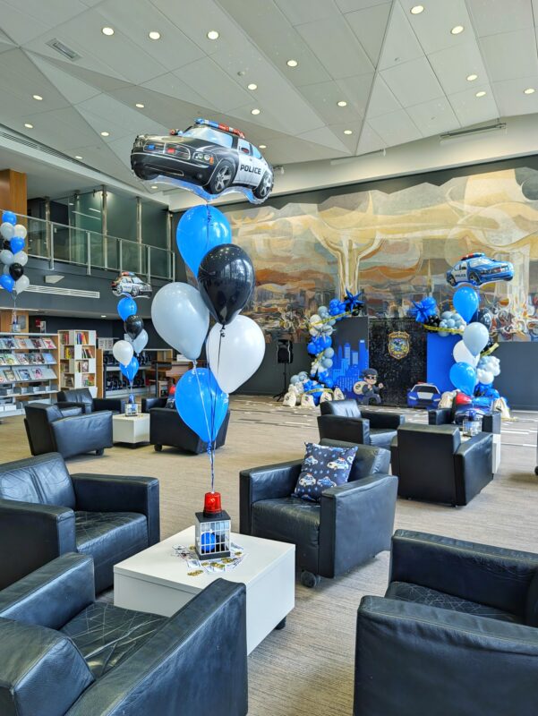 Police car helium balloon bouquet beside lounge seating and the themed birthday backdrop.