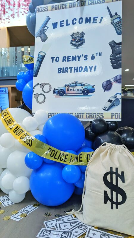 Police-themed welcome sign with blue, white and black balloons, caution tape and a money bag.