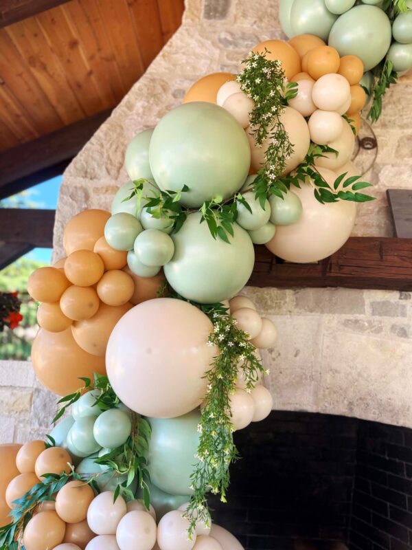 Close-up of sage green, peach, cream and tan balloons accented with soft greenery and flowers.