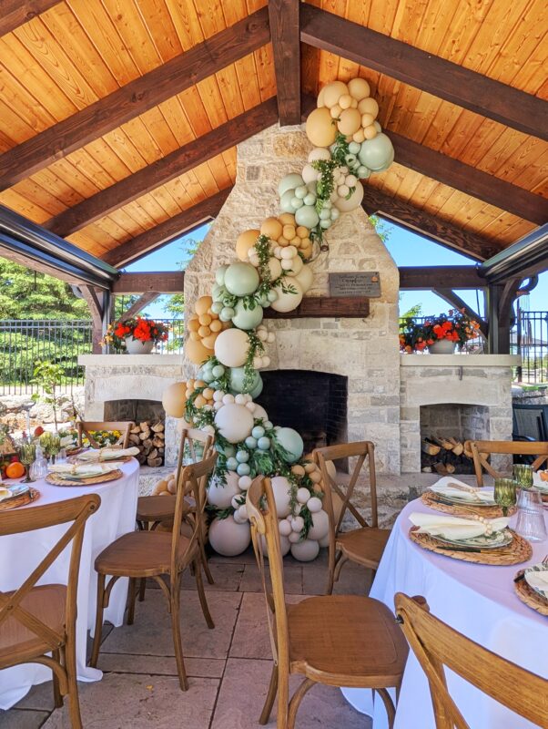 Stone fireplace framed by organic balloons behind garden-inspired backyard dining tables.