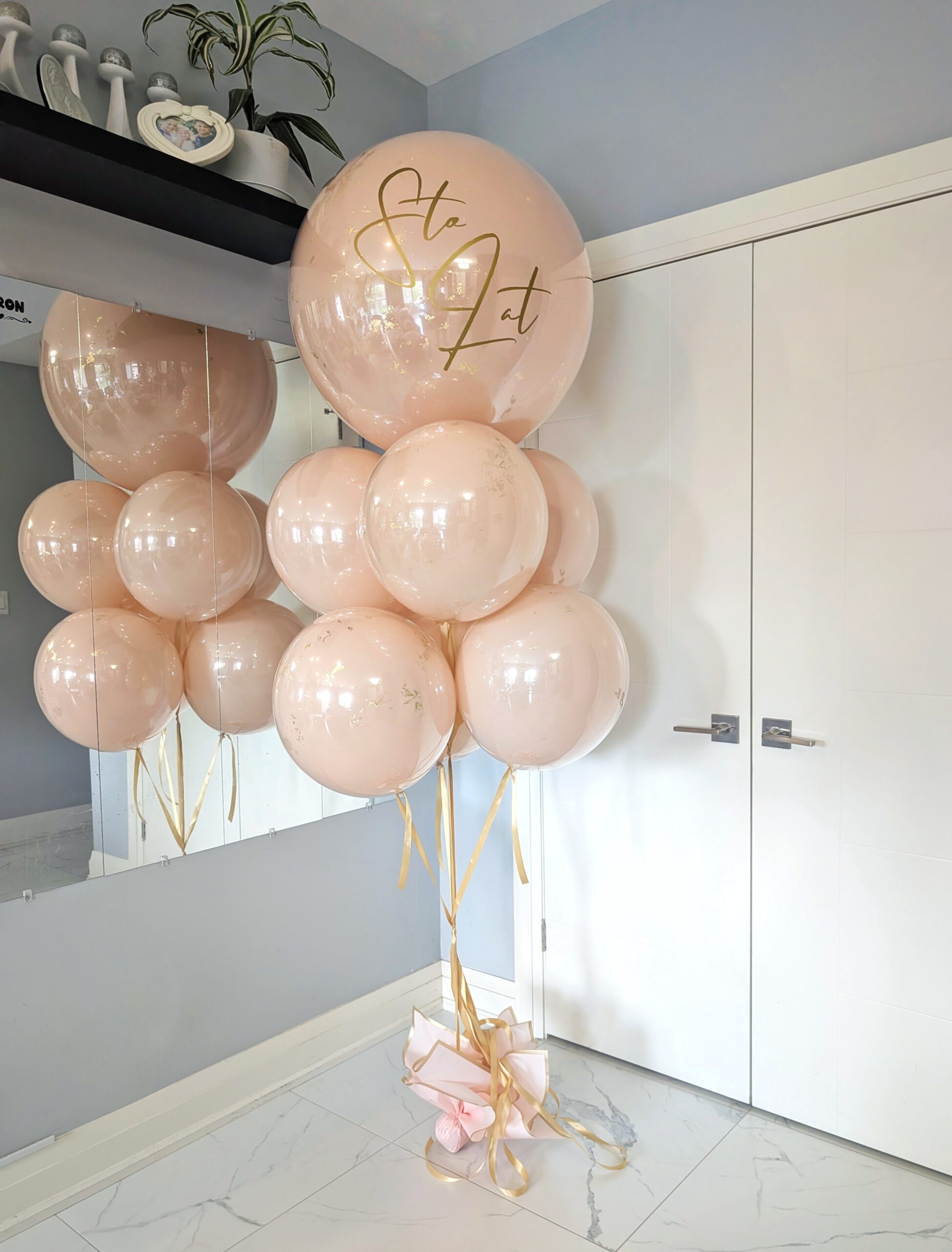 Personalized blush and gold bubble balloon bouquet with gold accents and coordinating blush-filled balloons.