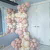Blush pink and ivory organic balloon garland arranged around a wall mirror with assorted balloon sizes.