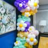 Pastel balloon garland with white daisies and purple, mint, blush and yellow balloons in a floor-to-ceiling display.