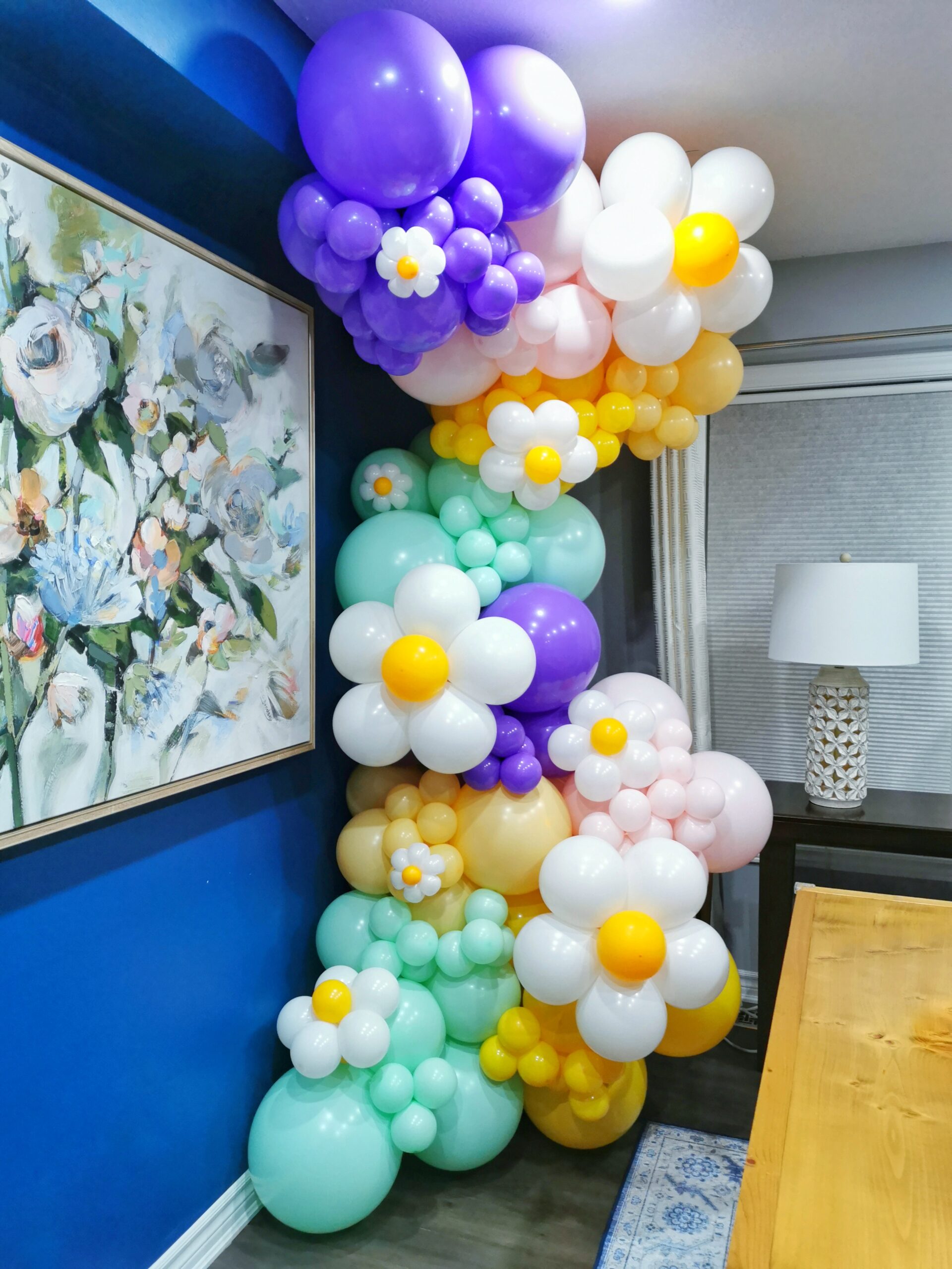Pastel balloon garland with white daisies and purple, mint, blush and yellow balloons in a floor-to-ceiling display.