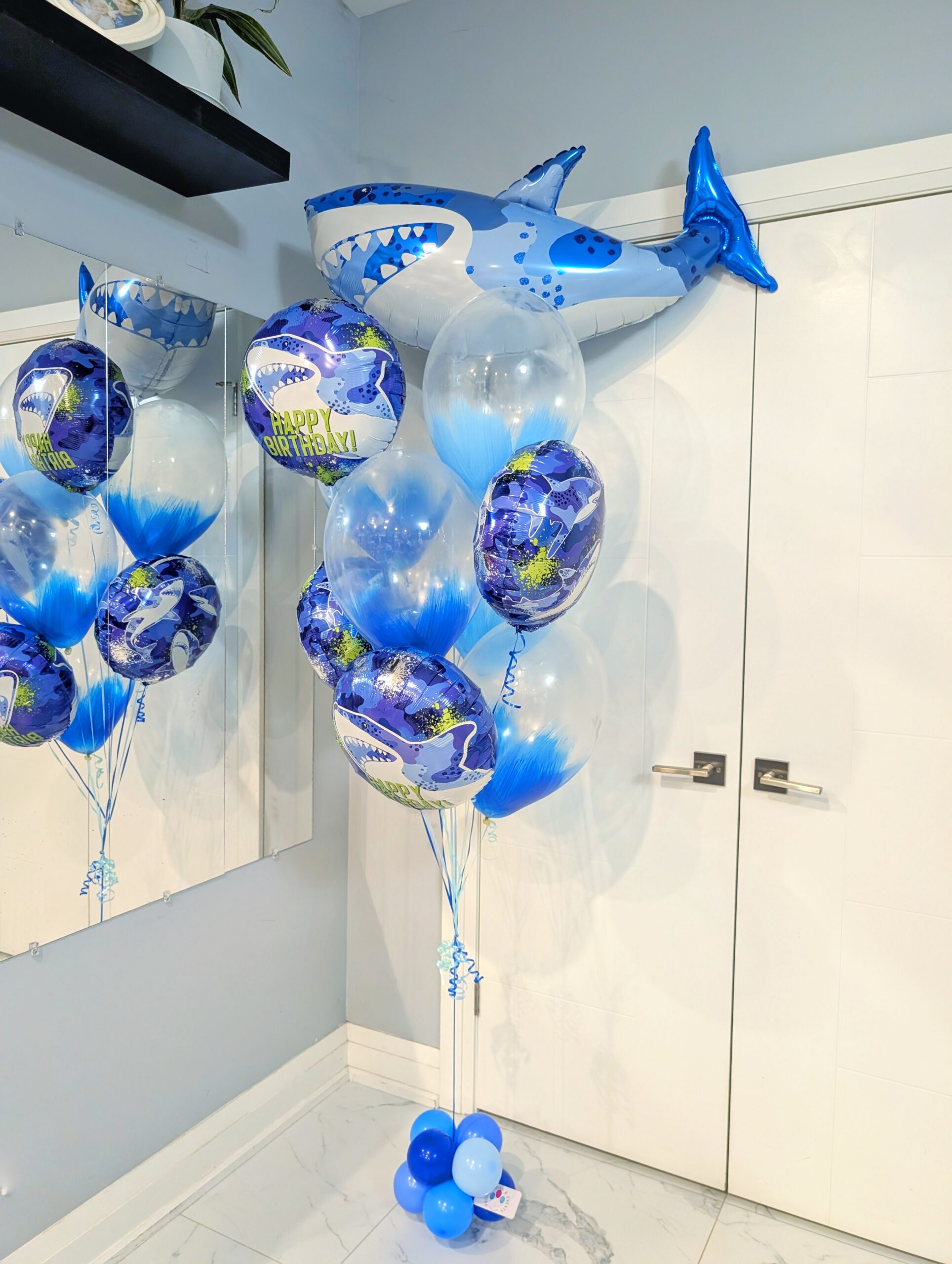 Blue shark birthday balloon bouquet with a giant shark foil and feather-filled clear balloons.
