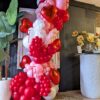 Red, pink and white balloon garland with metallic heart balloons, ribbon bows and sculpted accents.