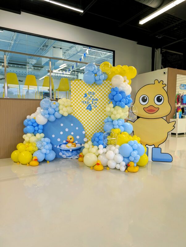 Blue, yellow, cream and white balloon installation framing a custom rubber duck backdrop.