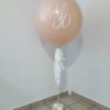 Personalized blush jumbo helium balloon with white lettering, tassels, and a coordinating balloon base.