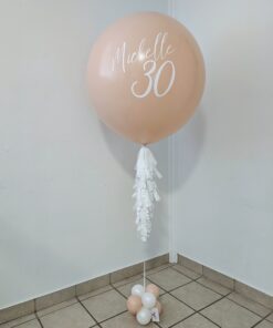 Personalized blush jumbo helium balloon with white lettering, tassels, and a coordinating balloon base.