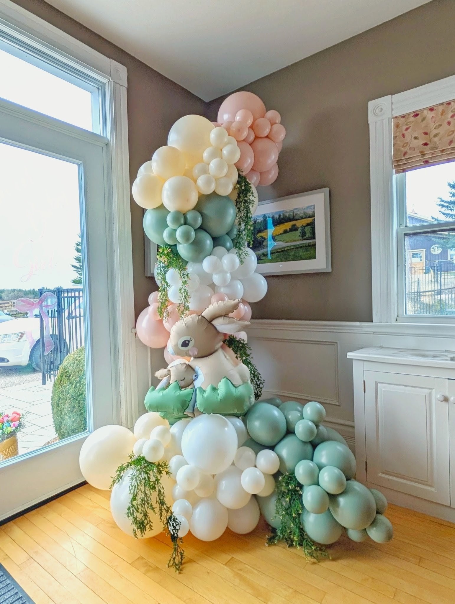Pastel bunny balloon column with blush, sage, ivory and white balloons, foil rabbits and cascading greenery.
