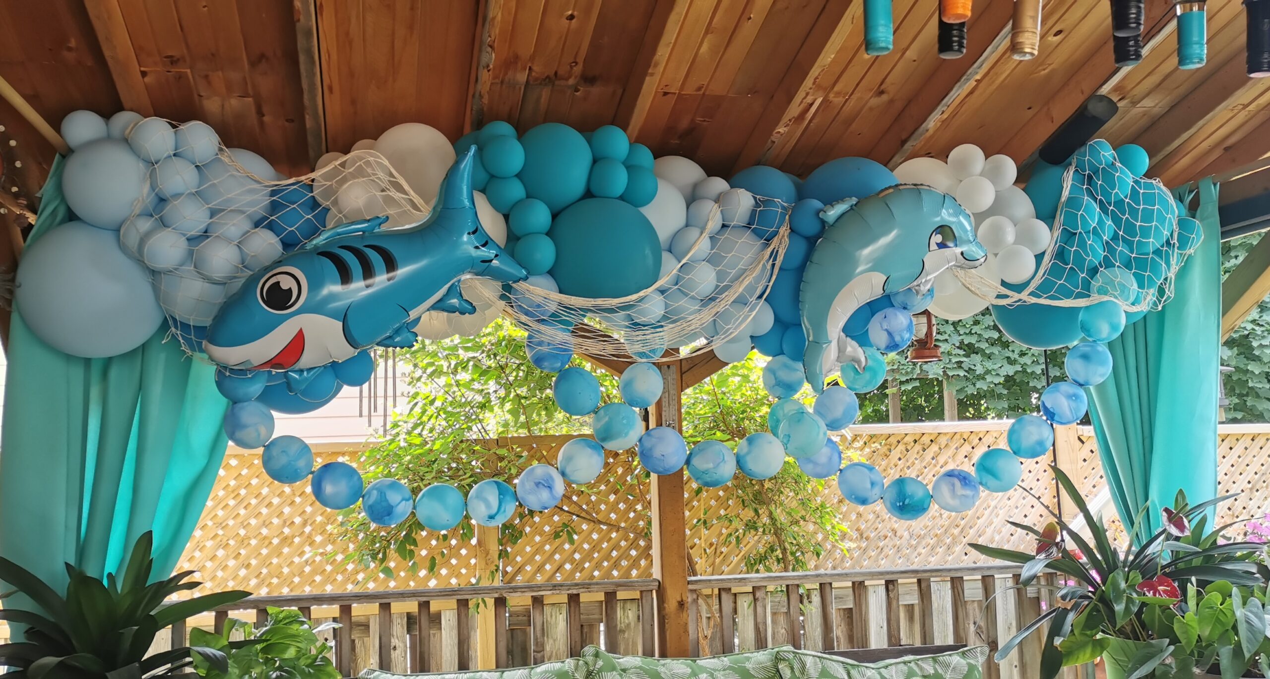 Blue under-the-sea balloon garland with shark and dolphin balloons, white accents and decorative fishing netting.