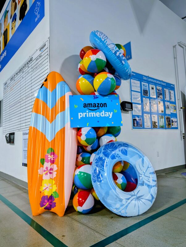 Amazon Prime Day beach display with a surfboard, swim ring, beach balls, and custom signage.
