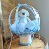 Clear stuffed balloon with a blue teddy bear, mini balloons, decorative shred, blue ribbons and a white base.