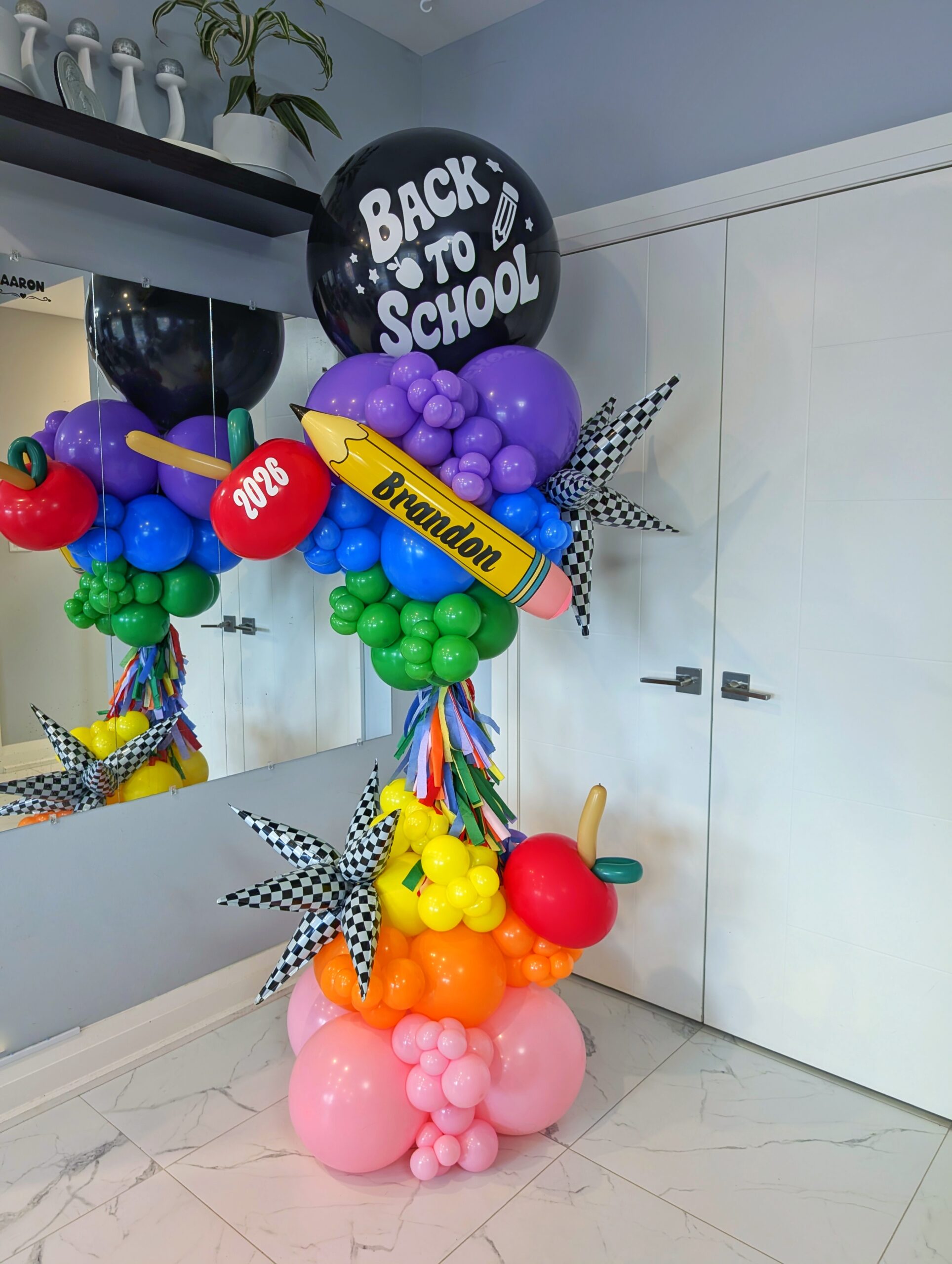 Rainbow Back-to-School balloon column with apples, starbursts, tassels and a personalized pencil.