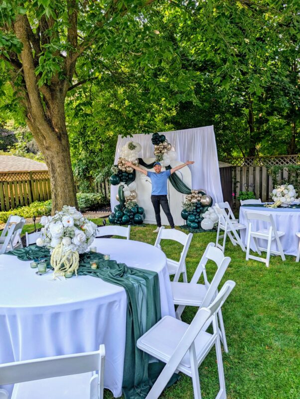 Complete backyard graduation styling with white tables, green runners and a balloon backdrop.