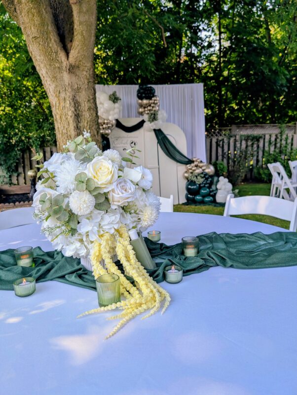 White faux floral centrepiece with trailing blooms on a deep green graduation tablescape.