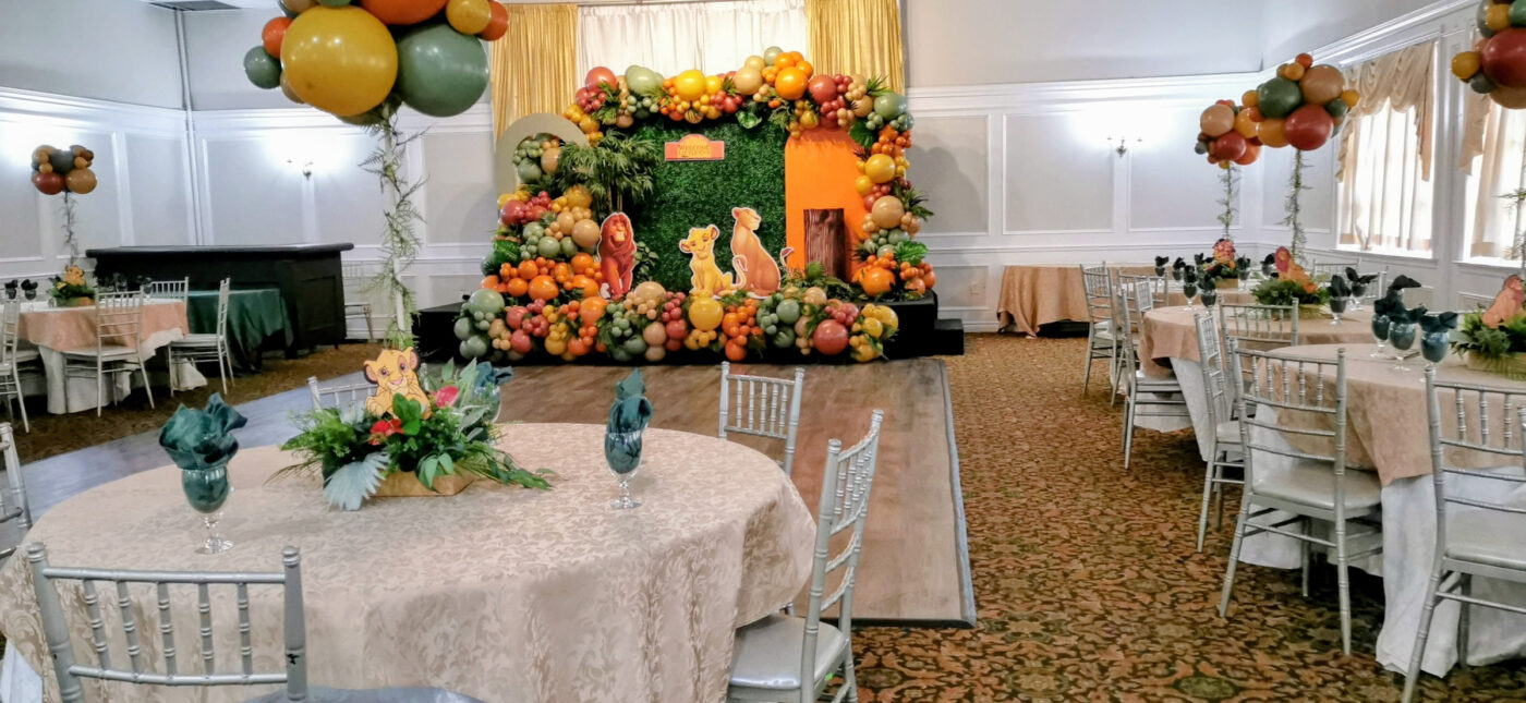 Wide view of Lion King baby shower room styling with table décor, balloon centrepieces and backdrop
