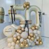 Gold and ivory anniversary number stack with black bows, balloon clusters, and a personalized name decal.