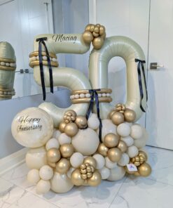Gold and ivory anniversary number stack with black bows, balloon clusters, and a personalized name decal.