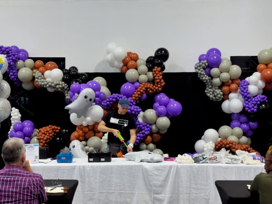 Instructor inflating a foil ghost beside the completed Halloween balloon garland