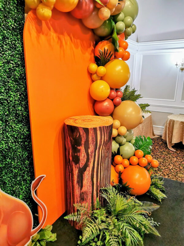 The custom tree-trunk plinth with orange backdrop and balloons and green foliage.