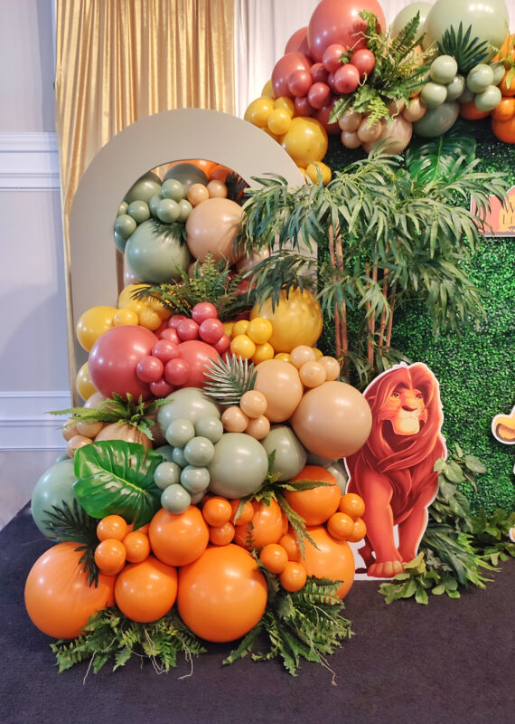Green hollow backdrop panel with custom tree-trunk prop, balloons and tropical greenery