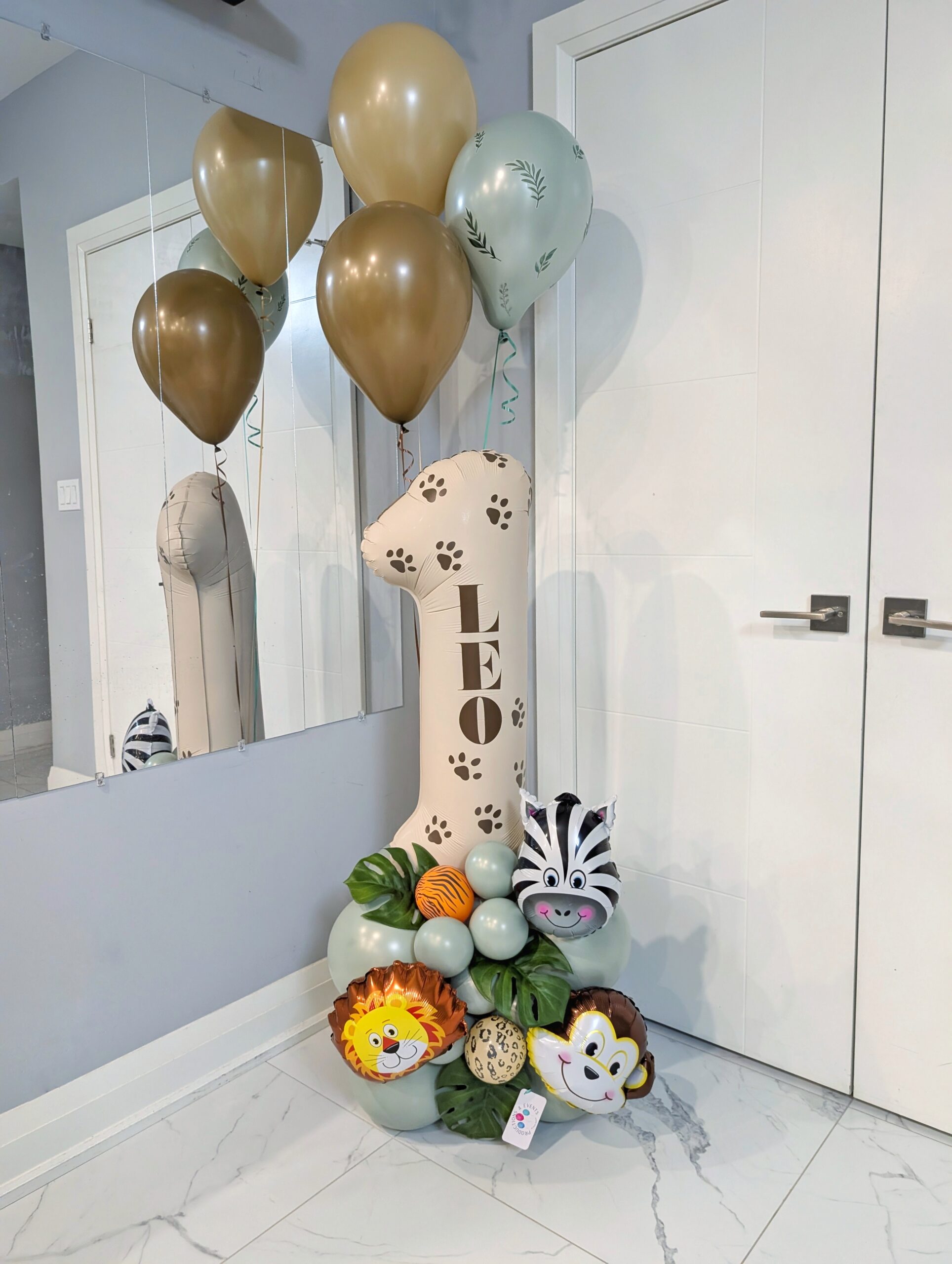 Safari birthday number stack with jungle animals, tropical leaves, sage balloons, paw prints, and a personalized name decal.