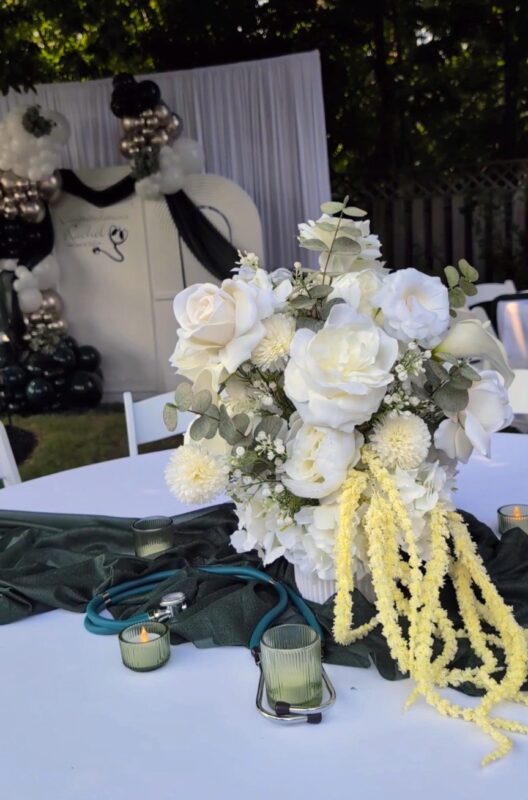 Medical-themed faux floral centrepiece with soft white flowers and deep green table accents.