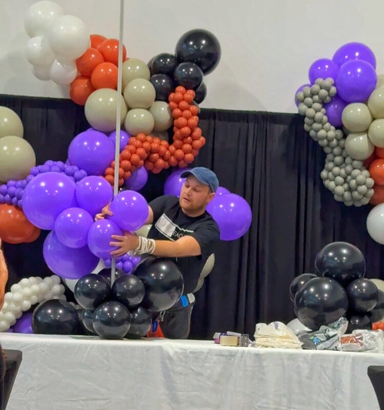 Instructor positioning purple balloon clusters on a freestanding garland frame