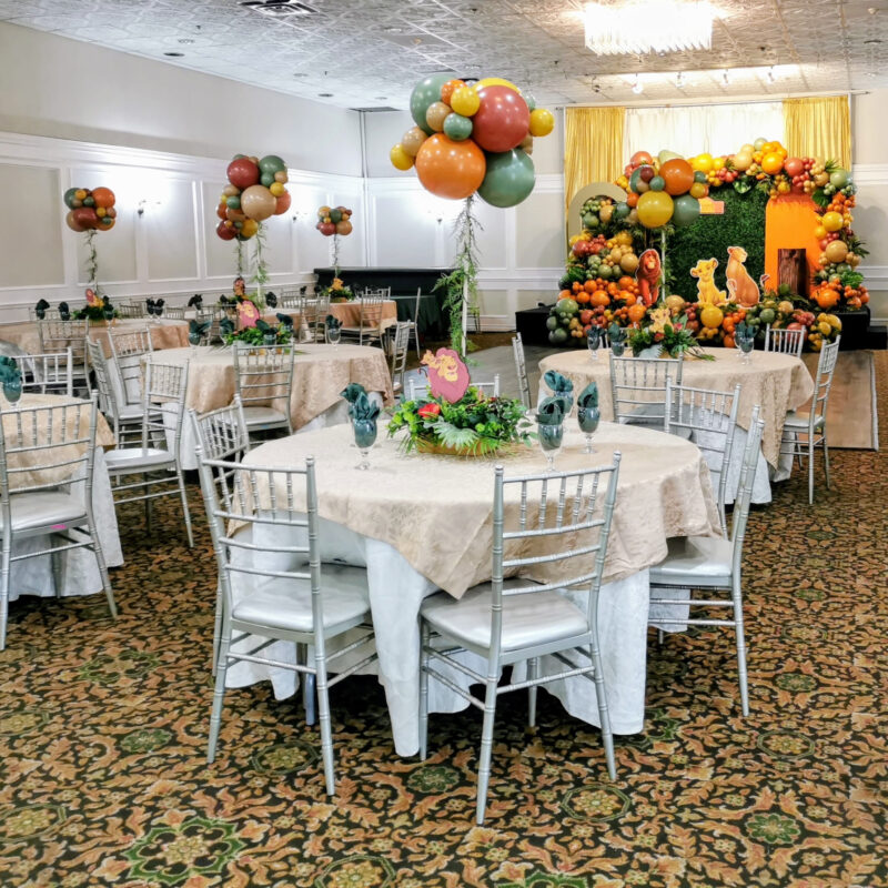 Styled baby shower table with floral centrepiece, green glassware and Lion King backdrop beyond