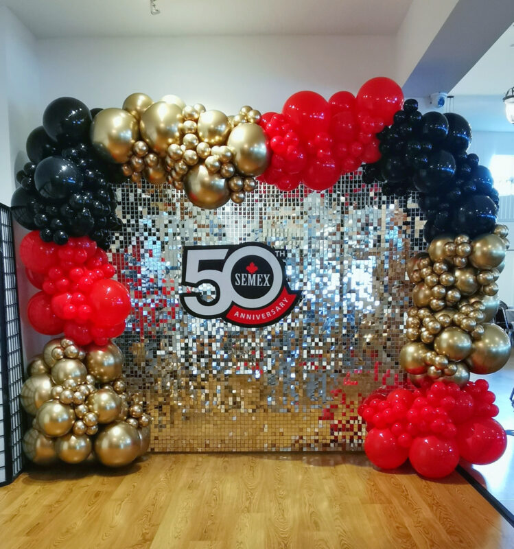 Organic red, black and gold balloon garland framing a shimmer wall with Semex 50th anniversary signage