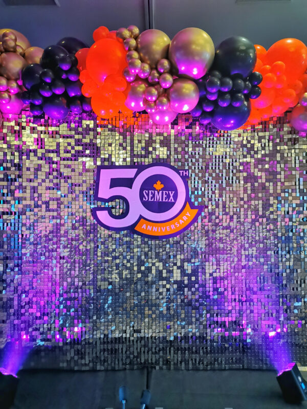 Semex 50th anniversary shimmer wall and balloon garland illuminated with purple stage lighting