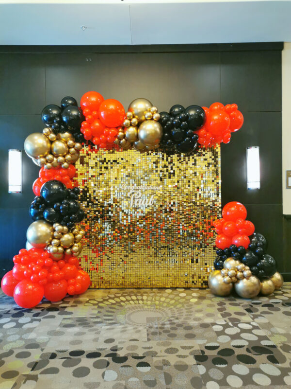 Gold shimmer photo backdrop with a red, black and gold balloon garland and Congratulations Semex sign
