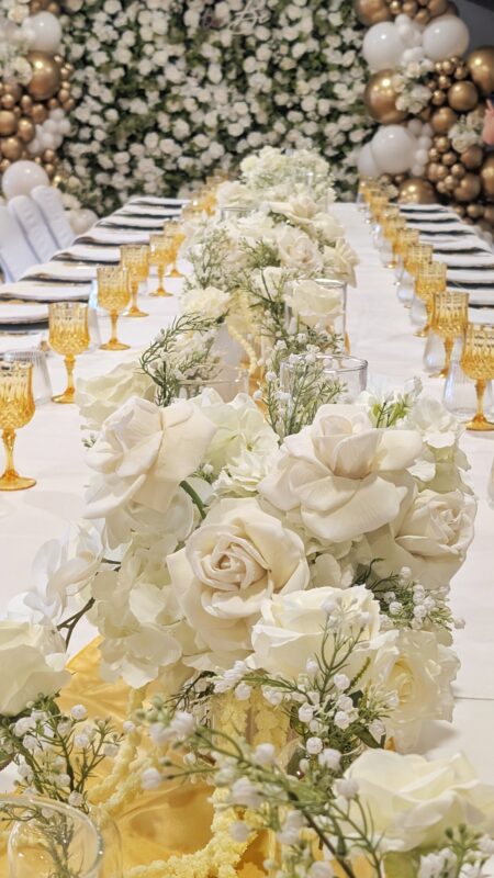 White faux floral centrepieces arranged along an elegant gold and white bridal shower table